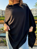 Woman wearing a black poncho outdoors with buildings and greenery in the background